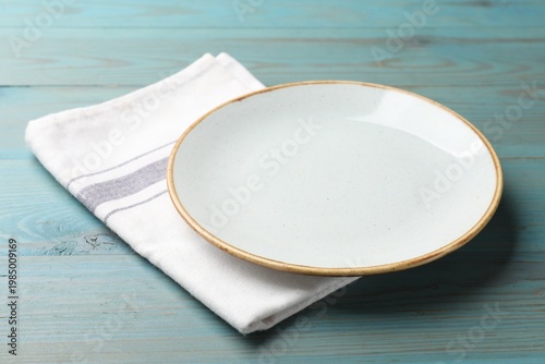 Empty plate and napkin on light blue wooden table, closeup