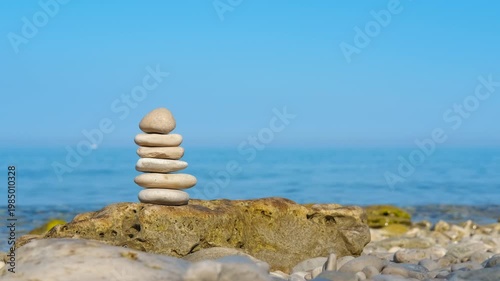 Zen stone cairn balancing on a sunny beach. Serene tower of balanced pebbles standing on a rocky seashore against the calm blue ocean and clear sky, symbolizing harmony, stability, meditation