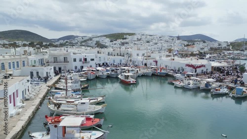 Aerial drone view of Easter celebration in Naousa village on Paros island, Greece, showing people gathered at outdoor tables in a festive Mediterranean atmosphere. Ideal for culture, travel, holidays
