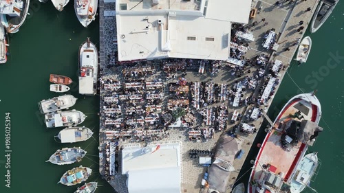 Aerial drone view of Easter celebration in Naousa village on Paros island, Greece, showing people gathered at outdoor tables in a festive Mediterranean atmosphere. Ideal for culture, travel, holidays