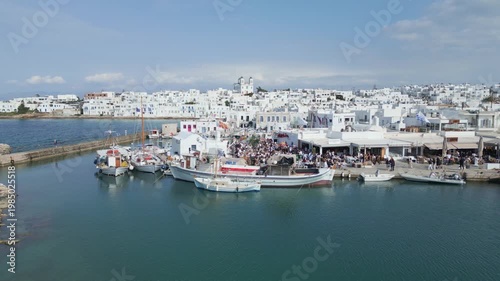 Aerial drone view of Easter celebration in Naousa village on Paros island, Greece, showing people gathered at outdoor tables in a festive Mediterranean atmosphere. Ideal for culture, travel, holidays
