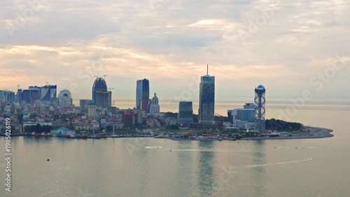 Batumi city skyline along the Black Sea coast at golden hour. Contemporary towers and seaside promenade with reflections on calm water, tranquil urban landscape.