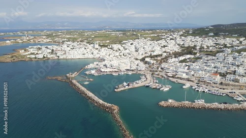 Aerial drone view of Naousa village on Paros island, Greece, showing traditional white buildings, coastal harbor and clear blue sea in daylight. Ideal for travel, tourism and Mediterranean lifestyle 
