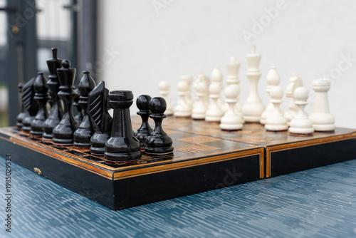 Quadro em tela Full chess set with black and white pieces arranged on decorative inlaid board outdoors on blue table with gravel background
