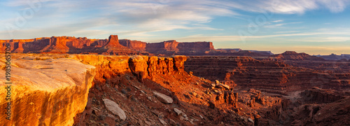 This scenic sunrise panorama from within Canyonlands National Park near Moab, Utah, features the sun's soft light at sunrise illuminating the inner canyon rim.