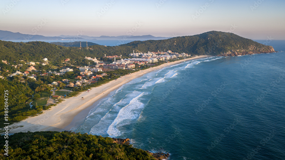 Fototapeta premium Empty Praia Brava at dawn with golden light, powerful waves and luxury condominiums on the hillside in Florianopolis.