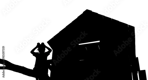 A silhouette of a person standing on a tree branch in front of a house
