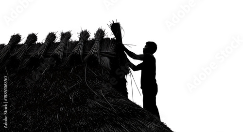 A silhouette of a man working on a thatched roof with bundles of straw