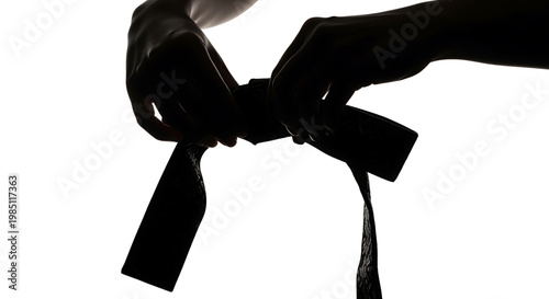 A person tying a black belt around their waist in a silhouette against a white background