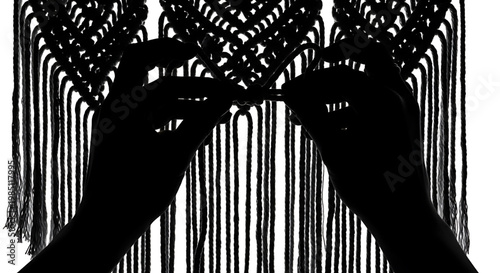A pair of hands in silhouette working on a macrame project with intricate knots and fringes
