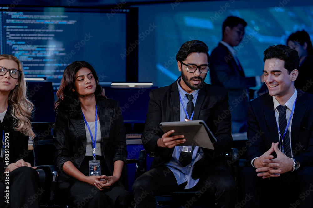 Obraz premium A large IT department meeting in a command center (SOC). An Indian analyst holds a tablet, listening with his team to a cybersecurity update on an AI system.