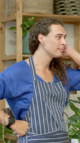 Vertical video: Hearing cue, plant florist in striped apron turning, touching ear, reaching plant
