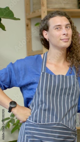Vertical video: Shifting chef adjusting pose while camera rolling in kitchen, with apron for camera