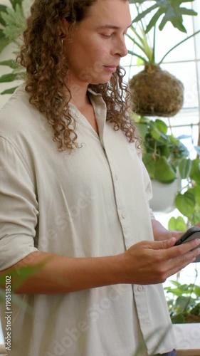 Vertical video: Checking messages on phone adult in beige shirt scrolling by window plants
