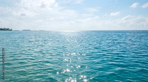 Sunlight sparkles on calm ocean waves near distant land on a cloudy day