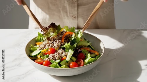 Person tossing fresh vegetable salad with quinoa in a ceramic bowl