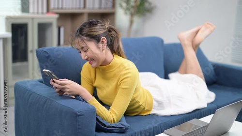 Young Woman Relaxing on Couch While Using Smartphone and Smiling