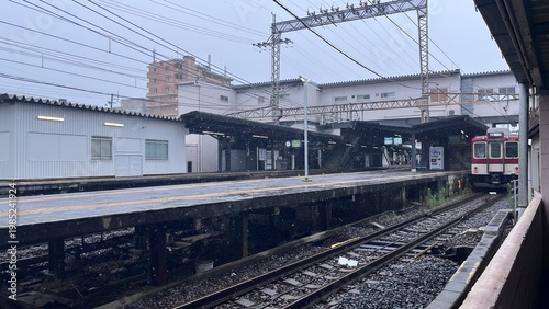 Kintetsu Railway train arriving at Fujiidera Station Platform 3 and 4 with overhead power lines and station infrastructure in rainy weather - Osaka, Japan, July 17, 2025