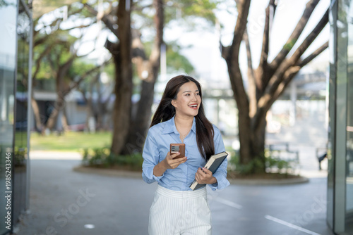 Slika na platnu Asian woman walking, holding book and smartphone