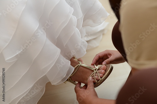 bride putting on golden sandal wedding shoe with ruffles, getting ready, closeup, bridesmaid hands helping bride put on gold sandal, wedding dress ruffles, wedding morning preparation, gold high heel 