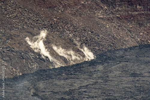 Steam rising from the base of a volcanic cliff where it meets the hardened lava floor in Hawaii Volcanoes National Park Hawaii