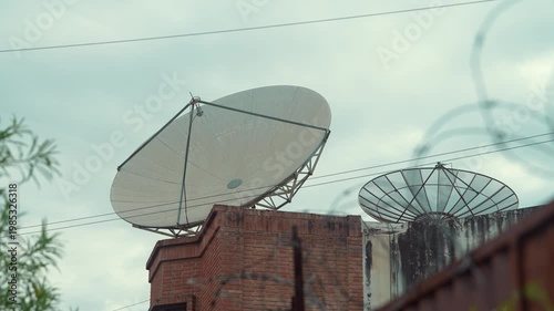 Two satellite dishes on rooftop with cables and overcast sky
