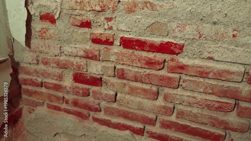 Exposed rough red brick wall with crumbling plaster and mortar
