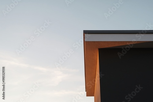 Roof edge of a dark modern structure is silhouetted against a pale evening sky during the twilight.
