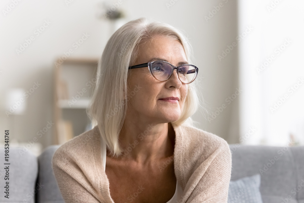 © fizkes - Beautiful pensive middle-aged woman wear glasses sit alone on couch and looking into distance with thoughtful, reflective expression, deep in thoughts, nostalgic mood, recollects, memories, close up