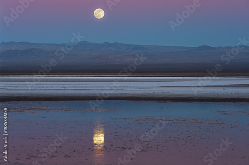 Full moon rising over Soda Lake in the Mojave Desert, mirrored in the shallow water as the Belt of Venus glows above the eastern horizon. Photographed at Zzyzx, California.