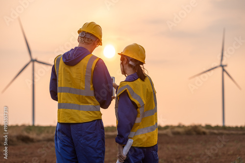 Tableau sur toile Engineer team using laptop at wind turbine farm during sunset, analyzing renewable
