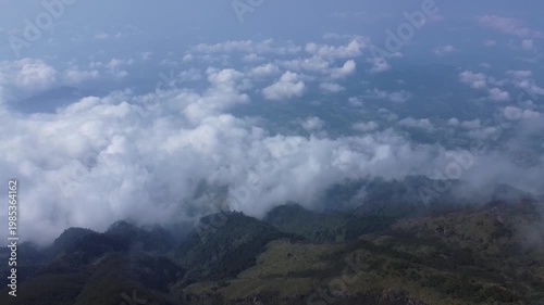 A breathtaking high-altitude drone shot captures a vast sea of white clouds rolling over the dark green ridges of Mount Sumbing
