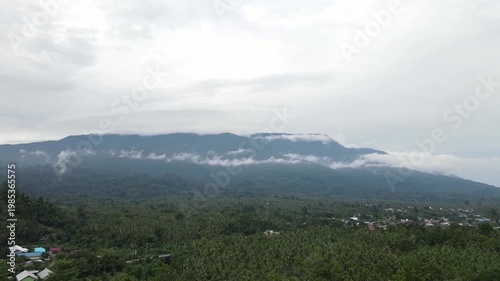 A majestic drone shot captures the pristine volcanic peaks of Halmahera, North Maluku, partially veiled by soft white clouds