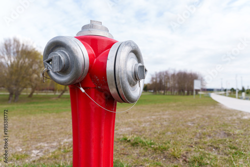 Modern red fire hydrant with silver caps and anti-tamper security seals, essential public safety equipment for fire protection and emergency water supply in a park setting
