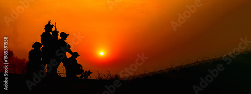 Foto Silhouetted soldiers in formation review tactical equipment and rifles against a dramatic fiery sunset, wearing camouflage uniforms and maintaining a somber, professional stance