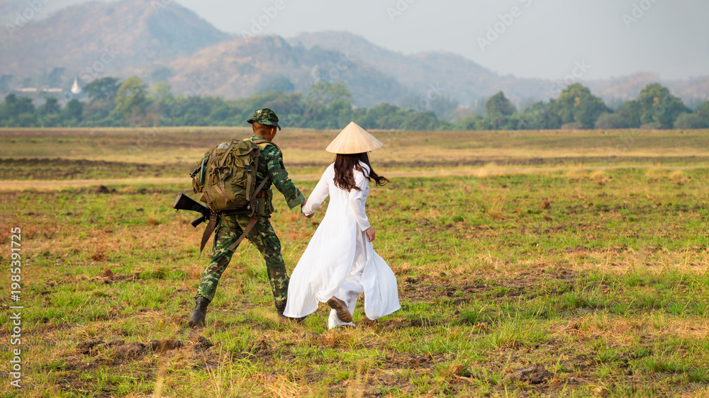 Obraz premium Soldiers and a Woman in White Dress Walking Across Grassy Field in Afghanistan Carrying Firearms and Backpacks, Creating a Somber Environment. A camouflage soldier and a woman wearing a white dres
