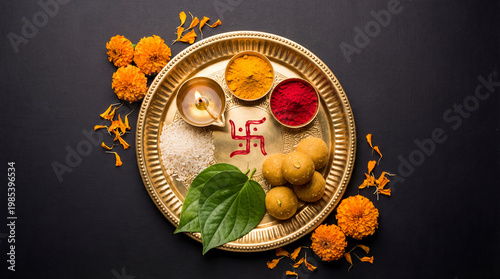 Close-up of a golden puja thali featuring a lit diya swastika symbol rice turmeric kumkum betel leaves and sweets with marigold flowers