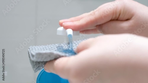 Female hands squeeze blue soap with dispenser close up on gray background.