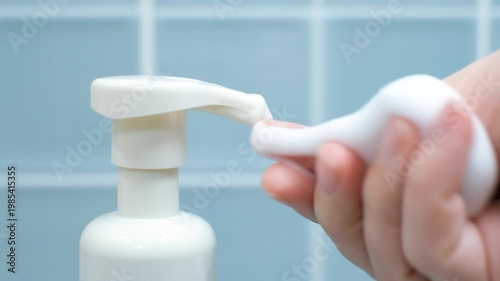 Female hand squeezing soap foam from black dispenser on blue background.