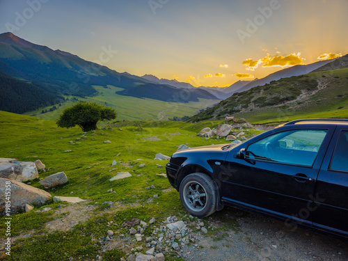Black station wagon car in serene mountainous landscape at sunset