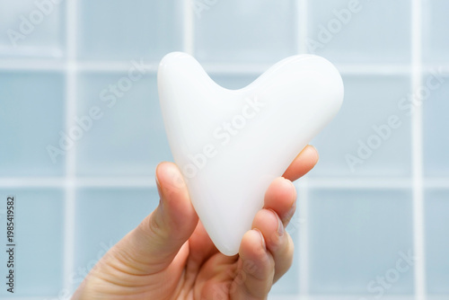 A hand holding gua sha face massager on blue background.