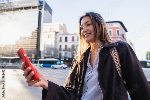 Young woman smiling holding red smartphone in city