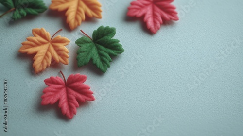 Stylized colorful artificial leaves are scattered across a textured surface with soft lighting. Image represents autumn themes, decorative elements, and seasonal background design.