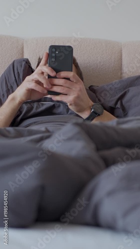 Man using smartphone in bed. Person lying in bedroom and holding mobile phone while lying under blanket. Concept of digital communication, social media and online leisure