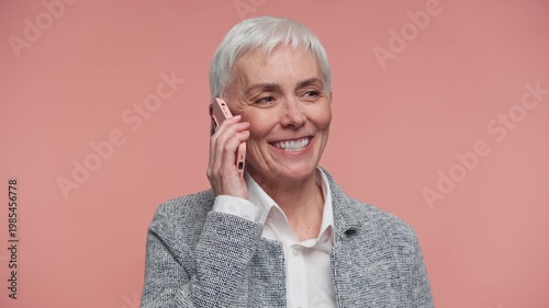 Smiling senior woman talking on phone on pink background