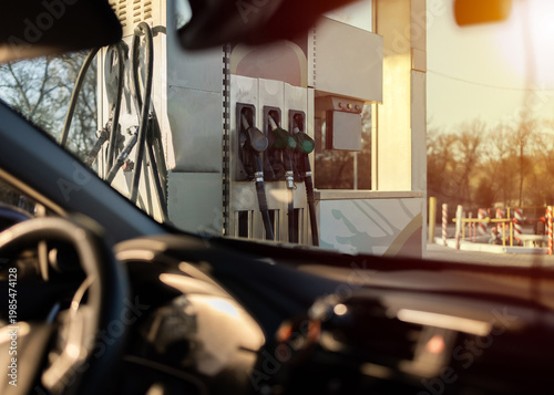 Man sitting in car at gas station during fuel crisis,checking empty wallet and holding payment card.Concept of rising fuel prices.Driver leaning on steering wheel.Close of fuel nozzle into car tank.