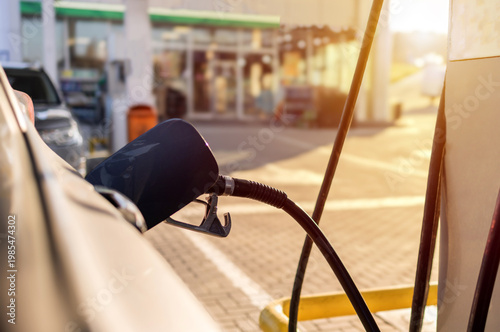 Man sitting in car at gas station during fuel crisis,checking empty wallet and holding payment card.Concept of rising fuel prices.Driver leaning on steering wheel.Close of fuel nozzle into car tank.