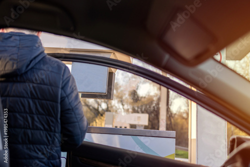 Man sitting in car at gas station during fuel crisis,checking empty wallet and holding payment card.Concept of rising fuel prices.Driver leaning on steering wheel.Close of fuel nozzle into car tank.