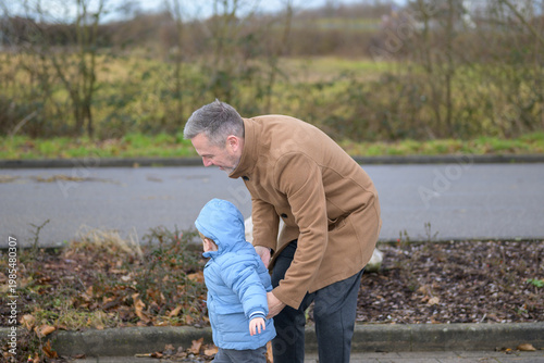 Grandfather Helping Toddler Walk Outside