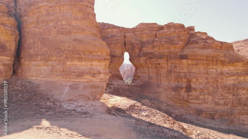 Couple travelers discover Saudi Arabia, they stand by the sandstone rock in AlUla, drone moves away from them, opening panorama of Arabic landscape in the desert